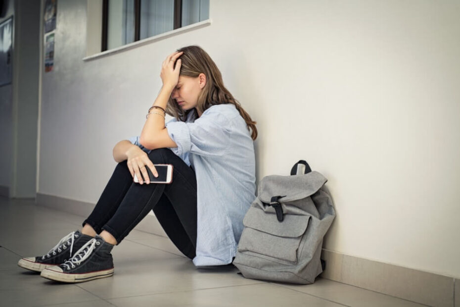 Traurige Studentin sitzt auf dem Boden